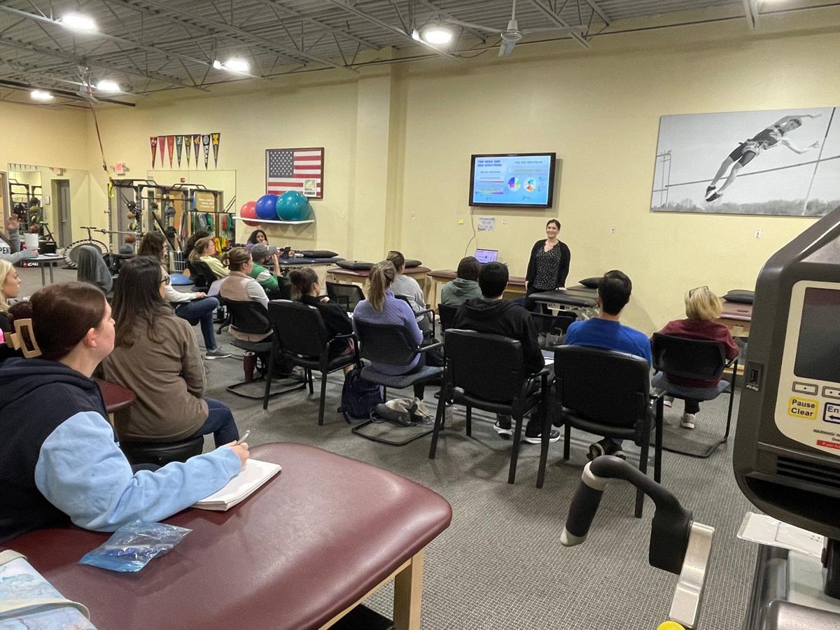 Val teaching a room of physical therapists at an outpatient clinic, with a slide on the hEDS and HSD spectrum