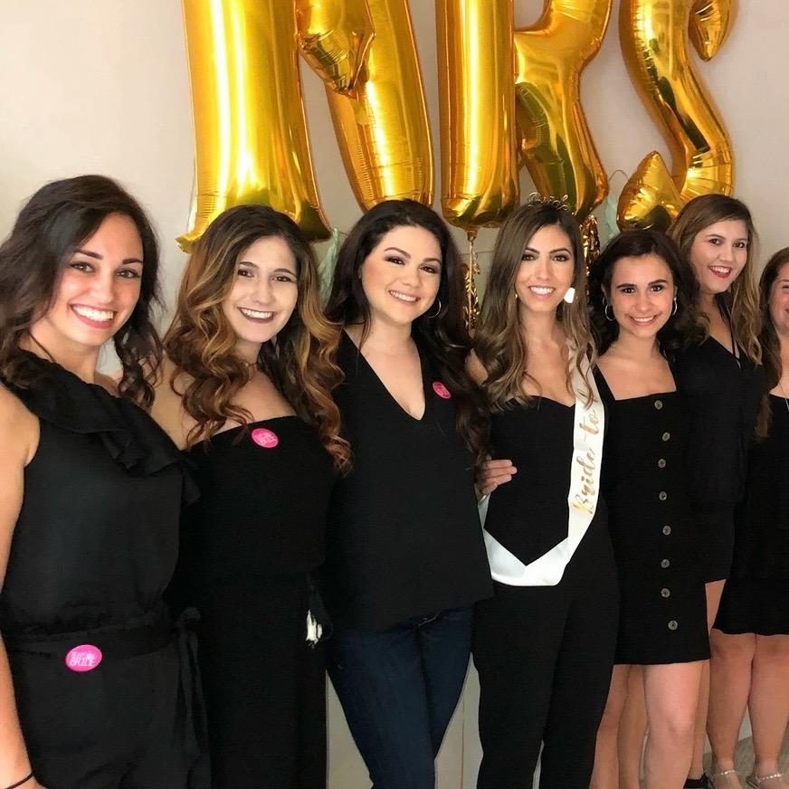 Val with her cousins at her bridal shower, all in black dresses under gold balloons
