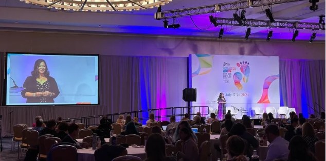 Val presenting to a packed ballroom at the 2024 Global Learning Conference, shown on the big screen
