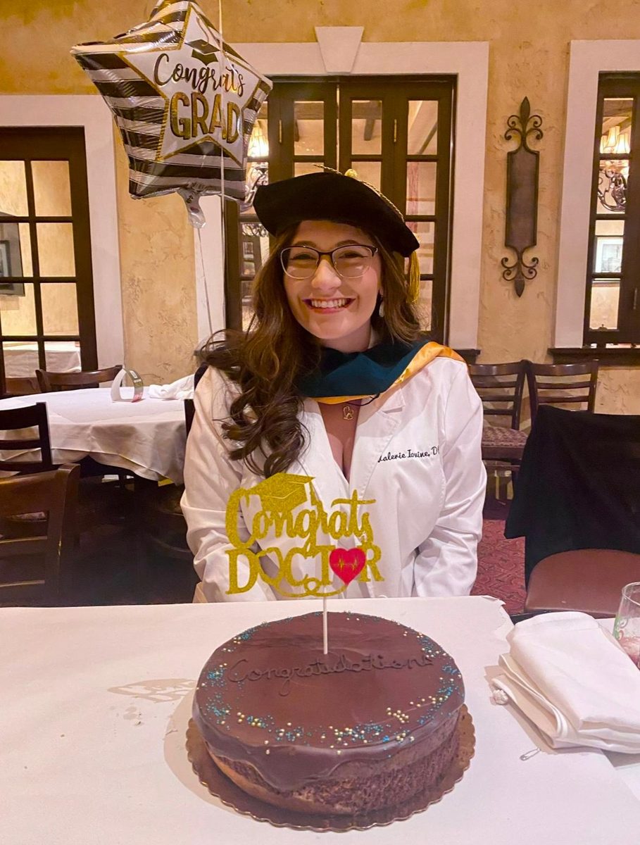 Val in her doctoral cap and gown with a Congrats Doctor cake